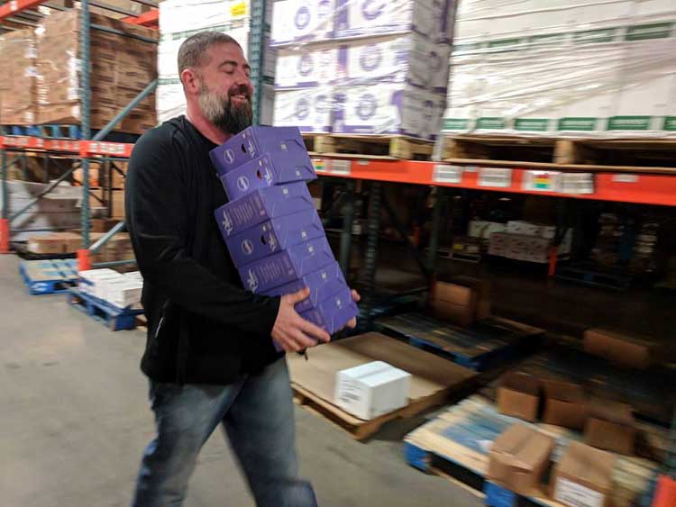 Tucker Smith of the Kansas City Dads Group carries a stack of Plum Organics baby food gift packages, bound for needy families, through the Harvesters Community Food Network warehouse during Giving Tuesday 2017 activities. (Photo: KC Dads Group)