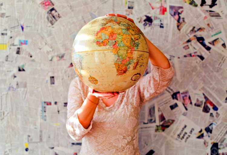 woman holds globe in front of headlines to find a balanced worldview