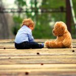 boy sits on deck with a teddy bar
