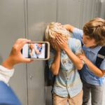 boy bullying other boy in hallway while someone records on smartphone