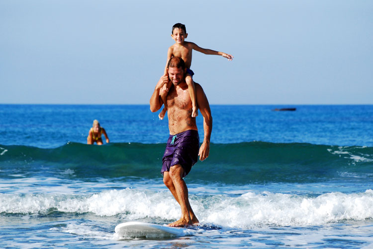 dad surfing with son on shoulders family vacation