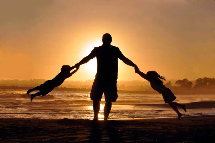 man swings children on the beach
