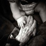 old person's hand reaches for baby's hand