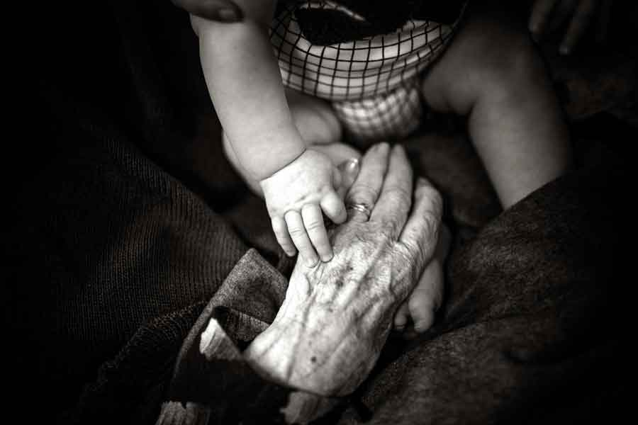 old person's hand reaches for baby's hand