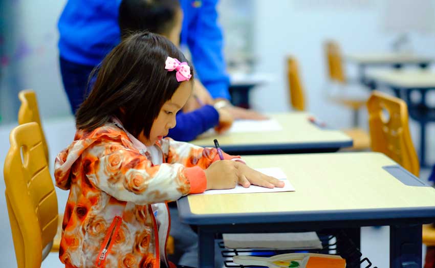 preschool student at school desk writes