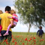 father carrying children through meadow
