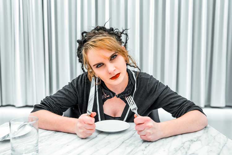 Thanksgiving conversations topics to avoid. Woman with knife and fork at table looks angry.