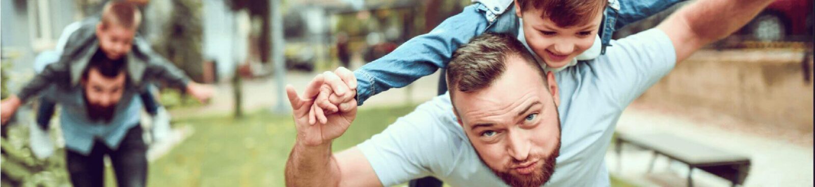 2 dads giving their kids piggy back rides with arms spread pretending to be airplanes 